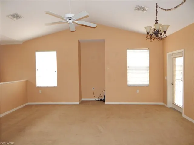 Unfurnished room with ceiling fan with notable chandelier, light colored carpet, and lofted ceiling