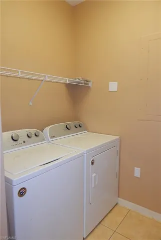 Laundry room featuring electric panel, washer and dryer, and light tile patterned floors