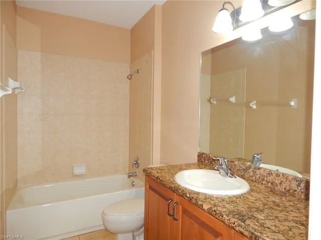 Full bathroom with tile patterned floors, vanity, tiled shower / bath combo, and toilet