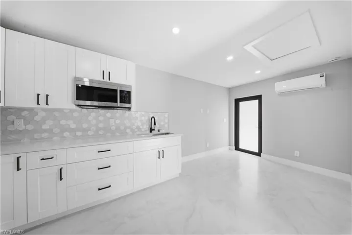 Kitchen featuring white cabinetry, light marble finish flooring, stainless steel microwave, a wall unit AC, and backsplash