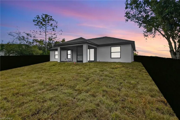 Back of property at dusk featuring stucco siding, a fenced backyard, a patio, and a shingled roof