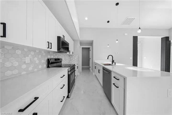 Kitchen with appliances with stainless steel finishes, white cabinetry, light stone counters, and hanging light fixtures