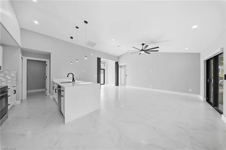 Kitchen featuring white cabinets, light stone counters, decorative light fixtures, vaulted ceiling, and light marble finish floors
