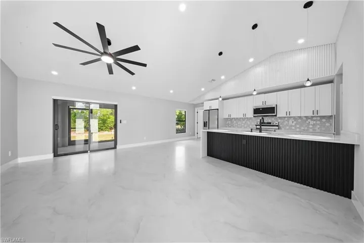 Kitchen featuring open floor plan, white cabinetry, lofted ceiling, healthy amount of natural light, and light marble finish floors