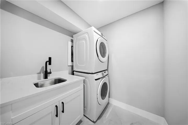 Laundry area with light marble finish flooring, stacked washing machine and dryer, and cabinet space