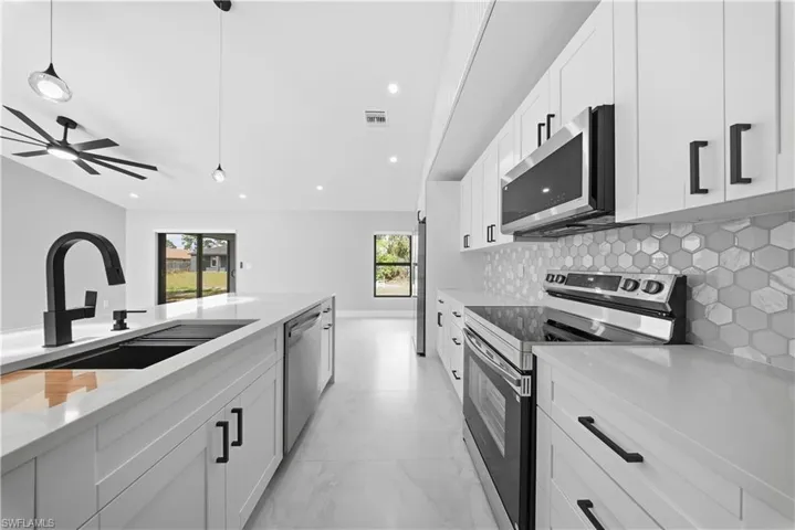 Kitchen with stainless steel appliances, white cabinetry, light marble finish floors, and light stone countertops