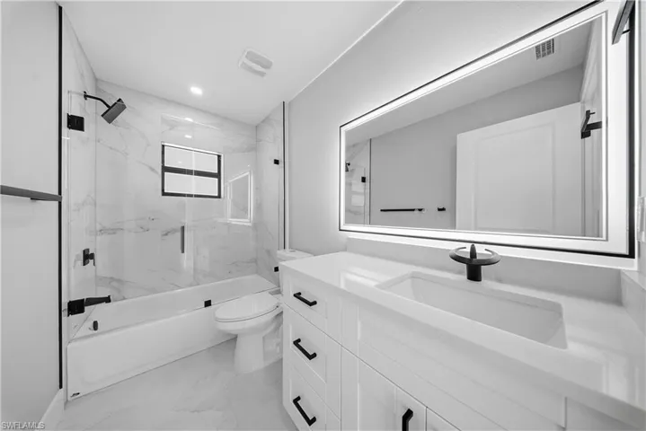 GUEST BATHROOM-Full bath with light marble finish floors, vanity, enclosed tub / shower combo, and recessed lighting