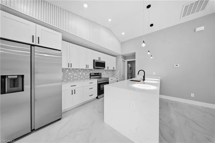 Kitchen with stainless steel appliances, light marble finish flooring, white cabinetry, decorative light fixtures, and light stone countertops