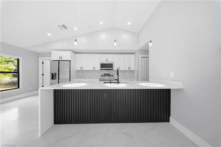 Kitchen featuring a peninsula, white cabinetry, light stone countertops, and vaulted ceiling