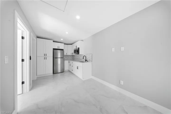 Kitchen with white cabinetry, stainless steel appliances, light marble finish floors, light countertops, and decorative backsplash
