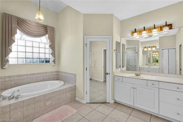Full bath featuring vanity, a stall shower, light tile patterned flooring, a garden tub, and a closet