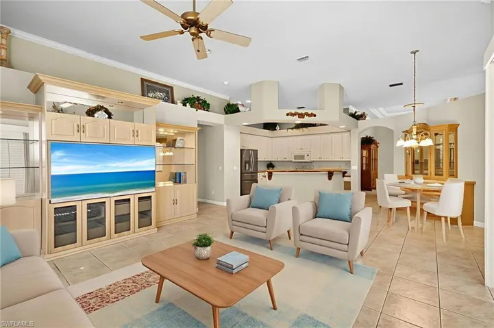 Living room with ceiling fan, arched walkways, light tile patterned floors, a chandelier, and crown molding