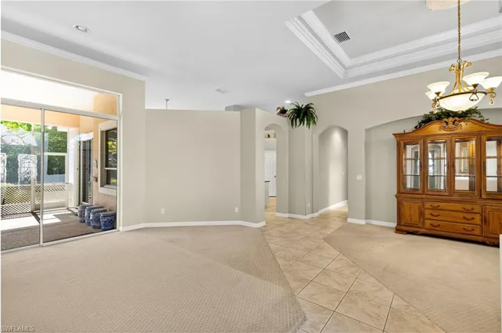 Unfurnished room with crown molding, light carpet, a chandelier, light tile patterned flooring, and arched walkways