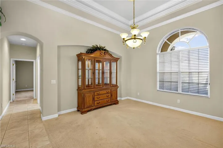 Spare room with light colored carpet, ornamental molding, arched walkways, a chandelier, and light tile patterned flooring