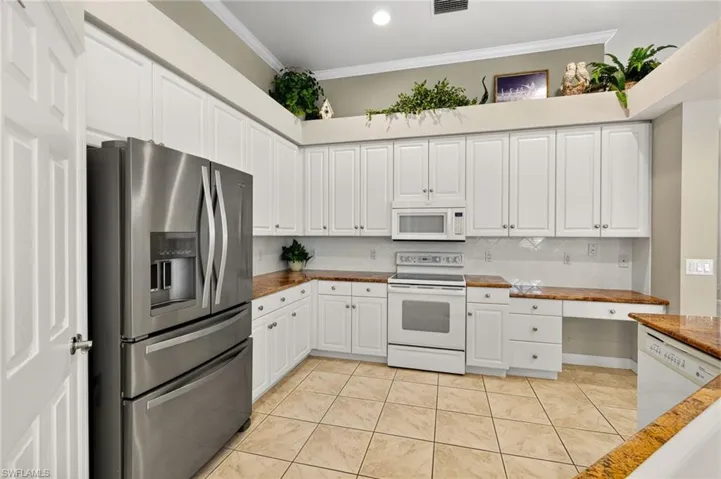 Kitchen with white appliances, white cabinetry, decorative backsplash, crown molding, and light tile patterned flooring