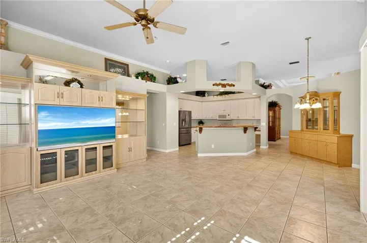 Unfurnished living room with a ceiling fan, arched walkways, a chandelier, light tile patterned floors, and crown molding