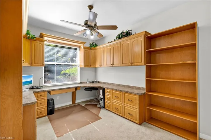 Unfurnished office with built in study area, light carpet, and a ceiling fan