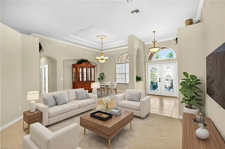 Tiled living area with crown molding, arched walkways, a raised ceiling, a chandelier, and french doors