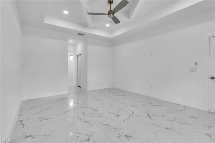 Empty room featuring light marble finish flooring, a raised ceiling, recessed lighting, and ceiling fan
