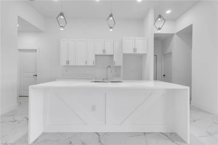 Kitchen with light marble finish flooring, a large island, white cabinets, recessed lighting, and decorative light fixtures