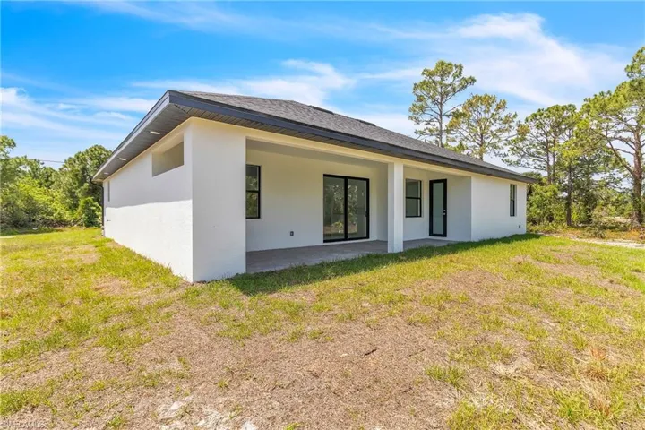 Back of property with stucco siding, a patio area, a yard, and roof with shingles