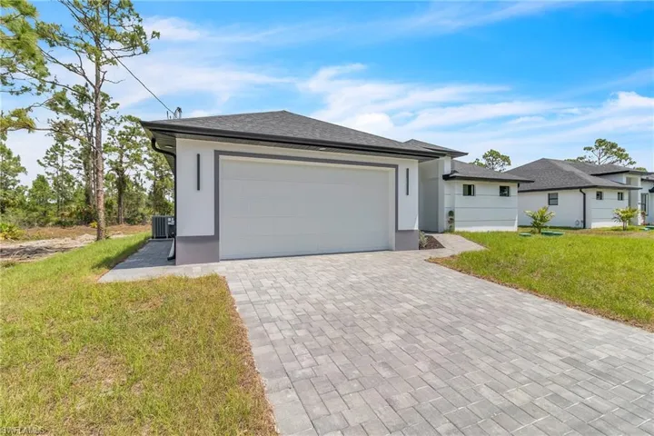 View of front of home featuring decorative driveway, a front lawn, stucco siding, and roof with shingles