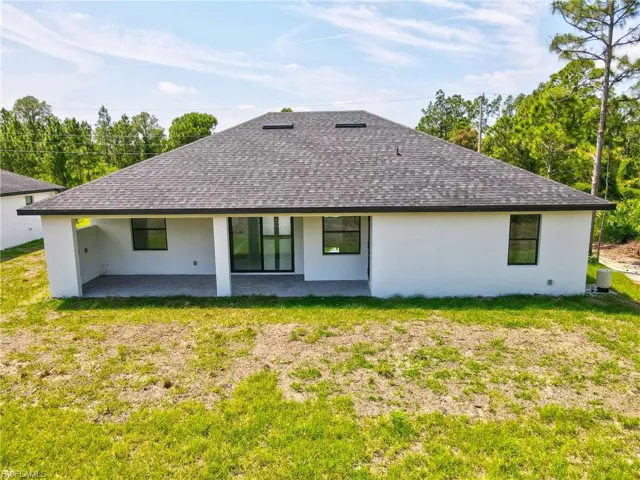 Rear view of property with a patio area, stucco siding, a yard, and roof with shingles