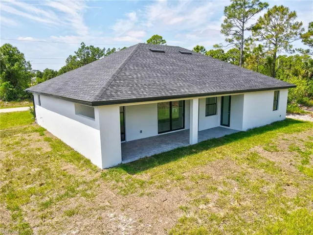 Rear view of house with a patio area, stucco siding, a lawn, and roof with shingles