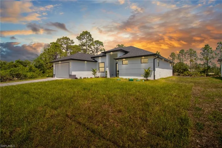 View of front of house with an attached garage, stucco siding, a front yard, concrete driveway, and a shingled roof