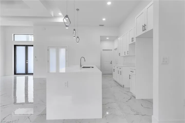 Kitchen with light marble finish flooring, white cabinetry, a center island with sink, decorative light fixtures, and recessed lighting