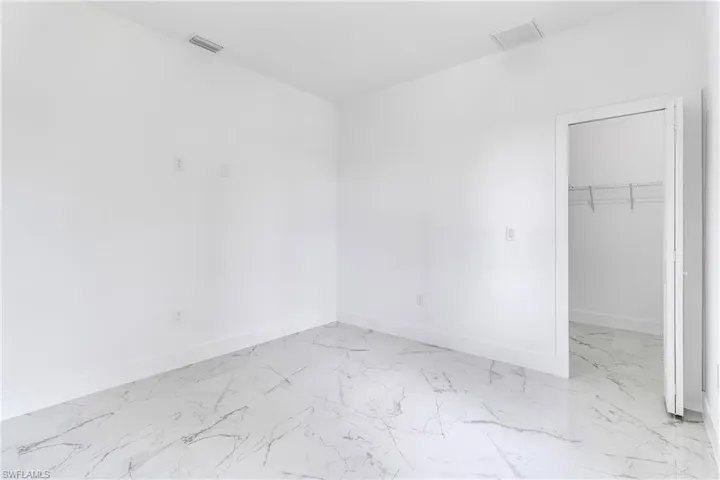Unfurnished bedroom featuring light marble finish floors and a walk in closet