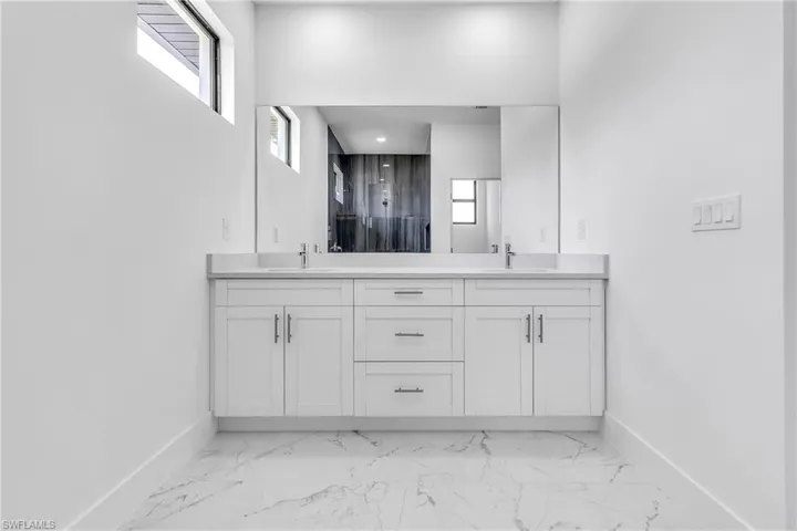 Bathroom featuring double vanity, marble look tile flooring, and a shower