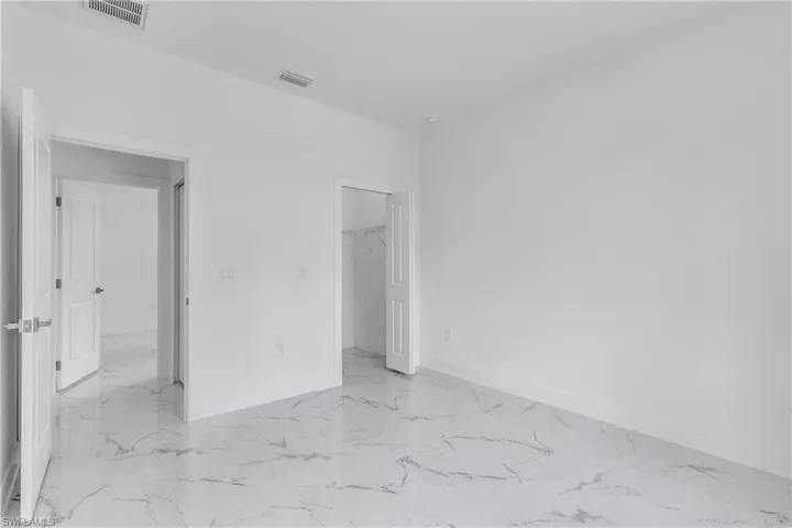Unfurnished bedroom featuring light marble finish flooring and a walk in closet