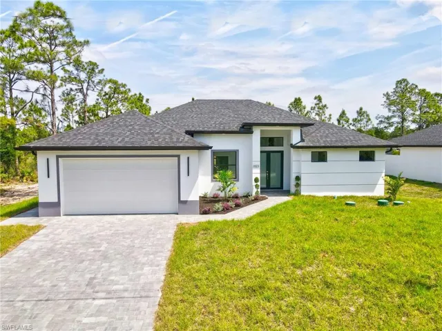 Prairie-style home featuring decorative driveway, a front yard, and stucco siding