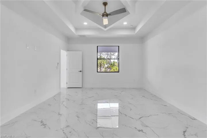 Empty room featuring light marble finish floors, recessed lighting, a tray ceiling, and a ceiling fan