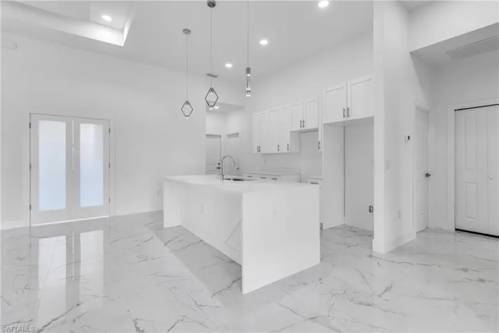 Kitchen with light marble finish floors, white cabinetry, french doors, a center island with sink, and recessed lighting