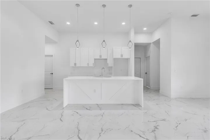 Kitchen featuring light marble finish floors, white cabinetry, a center island with sink, recessed lighting, and hanging light fixtures
