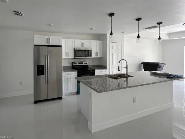 Kitchen featuring appliances with stainless steel finishes, white cabinetry, sink, dark stone countertops, and a kitchen island with sink
