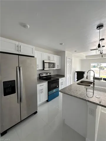 Kitchen featuring white cabinetry, appliances with stainless steel finishes, light stone countertops, and sink