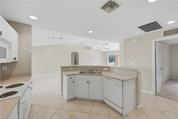 Kitchen with white cabinets, light countertops, white appliances, an island with sink, and vaulted ceiling