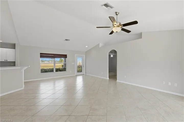 Unfurnished living room featuring arched walkways, vaulted ceiling, light tile patterned flooring, and ceiling fan
