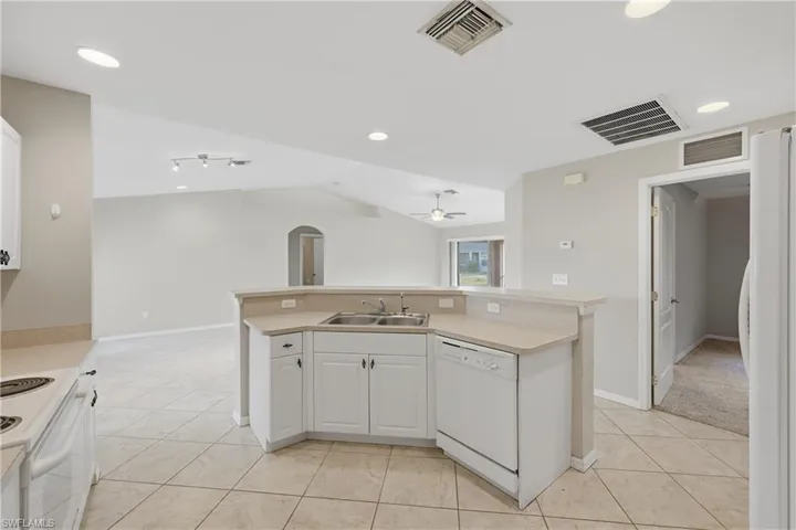 Kitchen with white appliances, white cabinetry, light countertops, lofted ceiling, and arched walkways