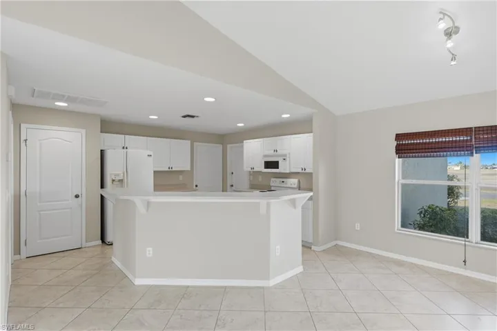 Kitchen with a kitchen breakfast bar, white cabinets, light countertops, vaulted ceiling, and a center island with sink