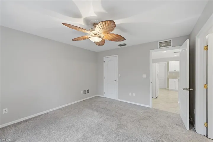 Unfurnished bedroom featuring light carpet, ceiling fan, and freestanding refrigerator