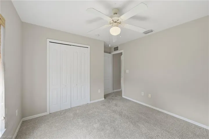 Unfurnished bedroom featuring light colored carpet, a closet, and a ceiling fan