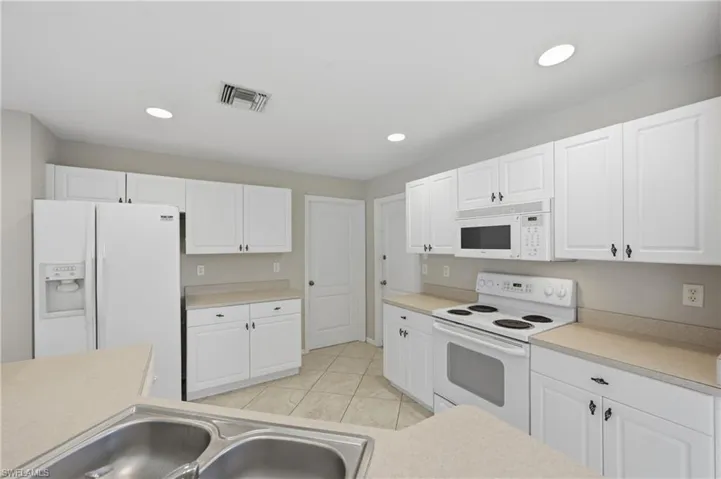 Kitchen featuring white appliances, light countertops, white cabinets, light tile patterned floors, and recessed lighting