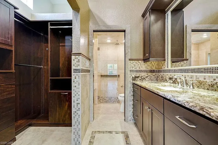 Bathroom featuring toilet, tiled shower, a textured wall, and vanity