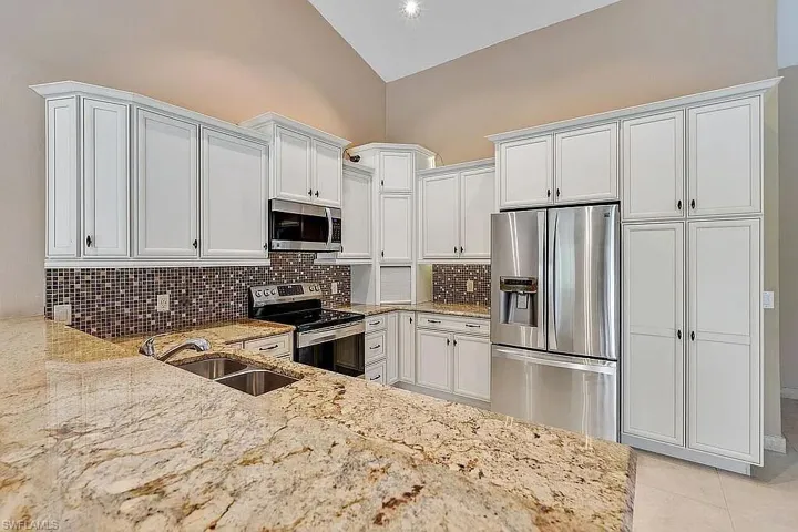 Kitchen featuring white cabinets, light stone counters, a sink, stainless steel appliances, and decorative backsplash