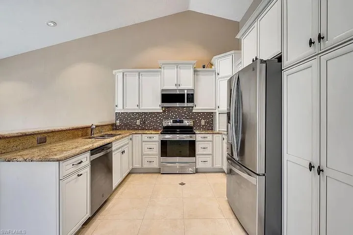 Kitchen with tasteful backsplash, vaulted ceiling, light stone countertops, appliances with stainless steel finishes, and a sink