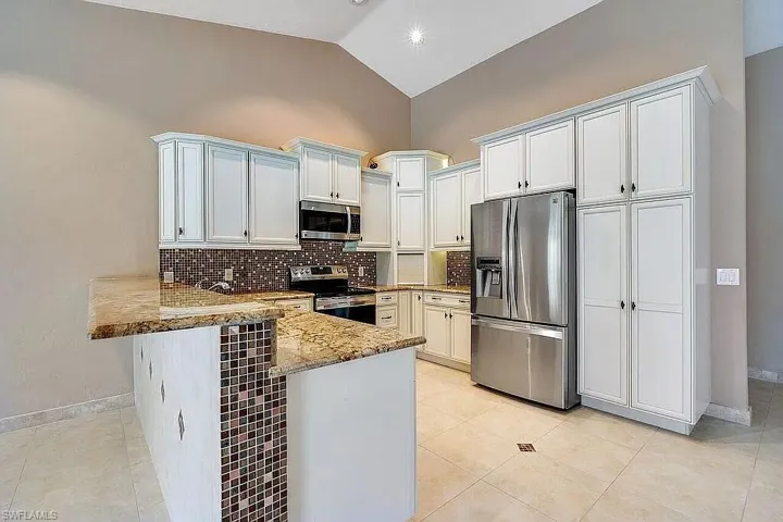 Kitchen with a peninsula, appliances with stainless steel finishes, baseboards, and light stone countertops